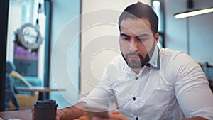 Handsome athletic man having a cup of coffee, while emailing with his phone, modern cafe. Social networks, being online