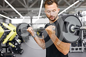 Handsome athletic man pumping up muscles with barbells