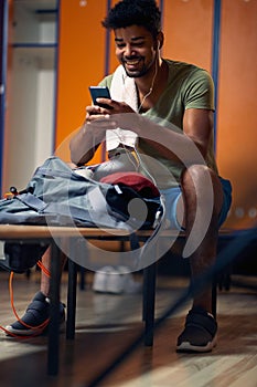 Handsome athletic man sitting in gym locker room, looking at phone, getting ready for workout photo