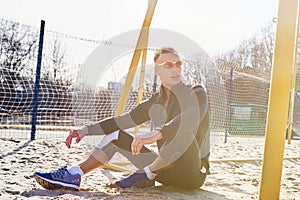 Handsome athletic man sitting on the sand field for beach soccer
