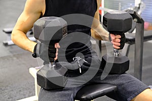 Handsome athletic man training his shoulders with dumbbells sitting on a bench in the gym