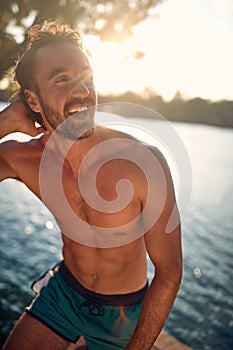 Handsome athletic man on wooden jetty by water. Young attractive man enjoying sun on vacation. Holiday, lifestyle, health concept