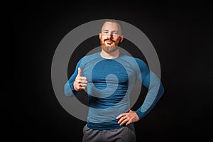 Handsome athletic muscular man showing a thumb up. Black background. Copy space. Sports advertising concept
