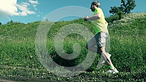 Handsome athletic sportsman running against green grass hill