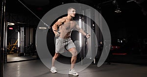 Handsome athletic young man doing exercises for biceps and abs using a modern expander. Full length.