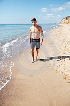 Handsome athletic young man walking along the beach