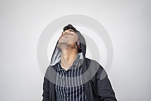 Handsome attractive indian man in black hoodie wear wireless music headphone,closed eyes feel the music standing against white