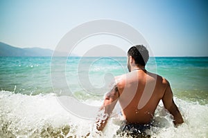 Handsome attractive muscular man sitting on sea shore on the beach sand and relaxing.Handsome man with tattoo sunbathing, spf