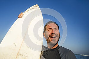 Handsome and attractive surfer man in neoprene swimsuit holding surf board posing cool after surfing enjoying Summer water sport