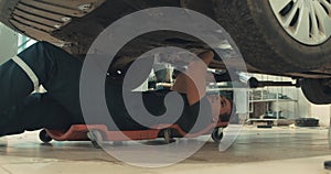 handsome auto mechanic working in garage lying under car repairing wheel