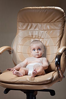 A handsome baby sitting in a overstuffed leather chair.