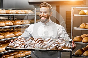 Handsome baker holding tray full of freshly baked croisants