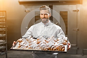 Handsome baker holding tray full of freshly baked croisants