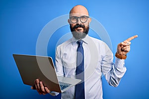 Handsome bald business man with beard working using laptop over blue background very happy pointing with hand and finger to the