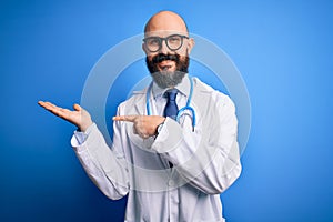 Handsome bald doctor man with beard wearing glasses and stethoscope over blue background amazed and smiling to the camera while