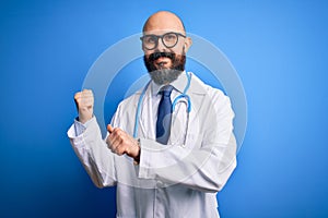 Handsome bald doctor man with beard wearing glasses and stethoscope over blue background Pointing to the back behind with hand and