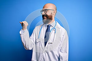 Handsome bald doctor man with beard wearing glasses and stethoscope over blue background smiling with happy face looking and