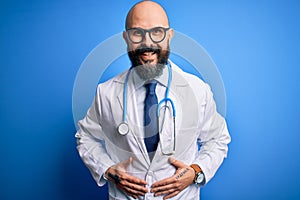 Handsome bald doctor man with beard wearing glasses and stethoscope over blue background smiling and laughing hard out loud