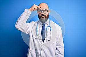 Handsome bald doctor man with beard wearing glasses and stethoscope over blue background worried and stressed about a problem with