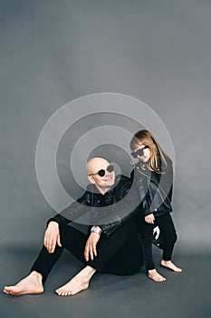 Handsome bald father with his little daughter in black sunglasses in biker clothes are posing in studio