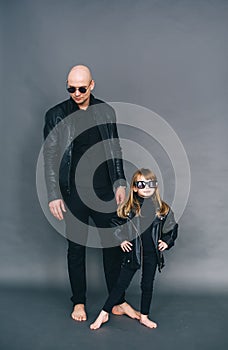 Handsome bald father with his little daughter in black sunglasses and in leather jackets are posing in studio