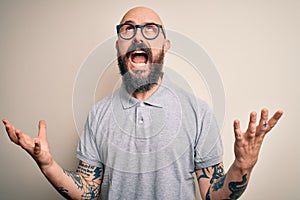 Handsome bald man with beard and tattoo wearing casual polo and glasses crazy and mad shouting and yelling with aggressive
