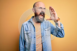Handsome bald man with beard wearing casual denim jacket and striped t-shirt shouting and screaming loud to side with hand on