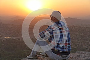 A handsome bald man in glasses sits on a sunset or dawn backgrou photo