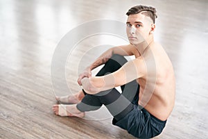 Handsome ballet dancer sitting on the floor and resting