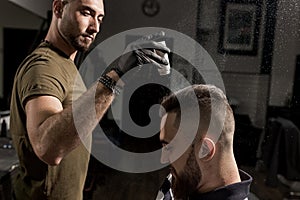 Handsome barber is fixing the styling of brutal young man with a dry styler at a barbershop