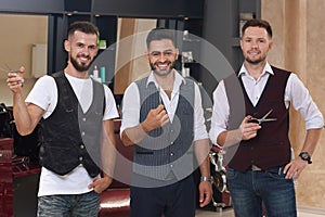 Handsome barbers posing with scissors and smiling.