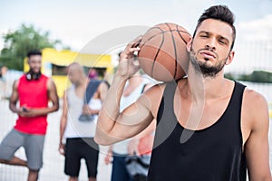 Handsome basketball player with ball on shoulder standing on court