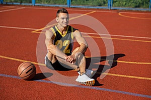 Handsome basketball player sitting on outdoor court