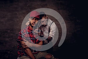 Handsome bearded African American guy in a fleece shirt and cap getting a haircut by an old-fashioned professional