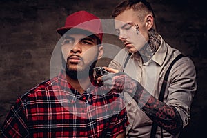 Handsome bearded African American guy in a fleece shirt and cap getting a haircut by an old-fashioned professional