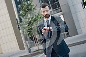 Handsome bearded businessman in classic suit is looking at his watch