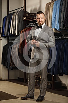 Handsome bearded businessman in classic suit. Man in classic vest against row of suits in shop