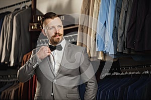 Handsome bearded businessman in classic suit. Man in classic vest against row of suits in shop