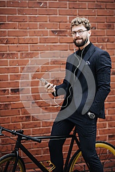Handsome bearded businessman in classic suit is using a smart phone for listen music and smiling while riding bicycle