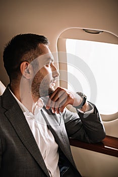 handsome bearded businessman looking at airplane window in private jet.