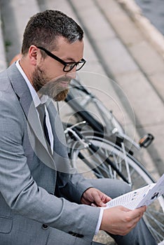 handsome bearded businessman reading newspaper on stairs