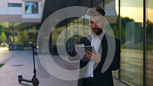 Handsome bearded caucasian man using digital tablet, near the business centre texting, scrolling apps.