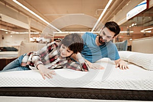 Handsome bearded father with young son is testing mattress for softness.