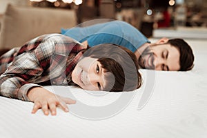 Handsome bearded father with young son is testing mattress for softness.