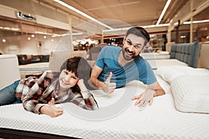 Handsome bearded father with young son is testing mattress for softness.