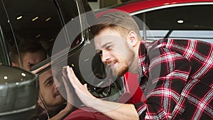 Handsome bearded male customer examining car paint on a new auto at the dealership