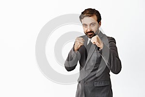 Handsome bearded male entrepreneur, businessman in suit raising clenched fists ready to fight, defensive pose, standing