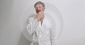 Handsome bearded man with blue eyes in white bathrobe touching beard