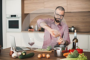 Handsome bearded man cooking vegetable stew using laptop