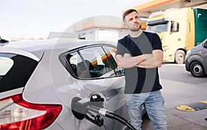 Handsome bearded man cross the arms during refueling car. Male looking on the scoreboard at gas station